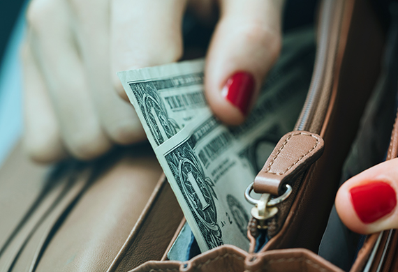 The girl's hand takes out paper dollars from a leather orange purse. Crisis and economy concept. Close-up.